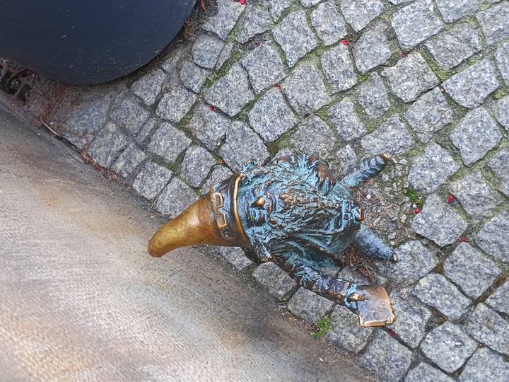 Small bronze gnome statue wearing a pointed hat on a cobblestone pavement.