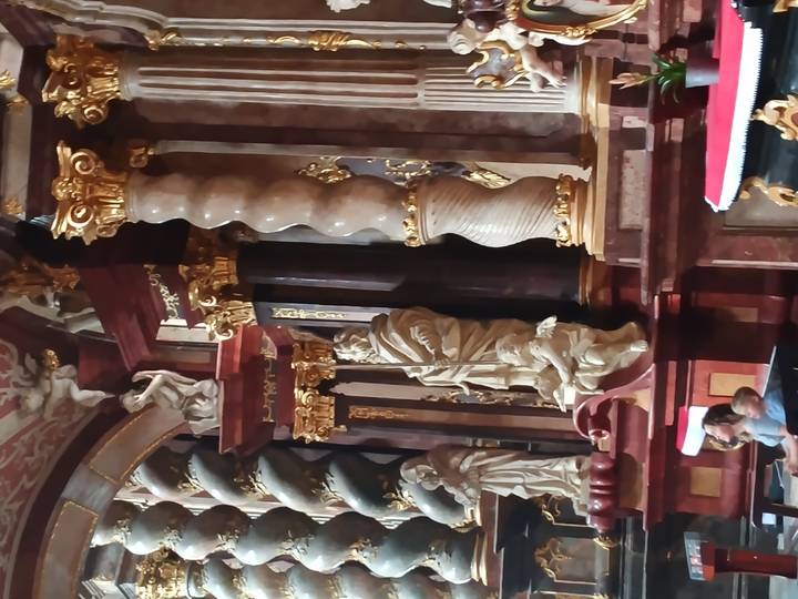 Opulent baroque church interior with twisted marble columns, gilded statues and a richly decorated altar.