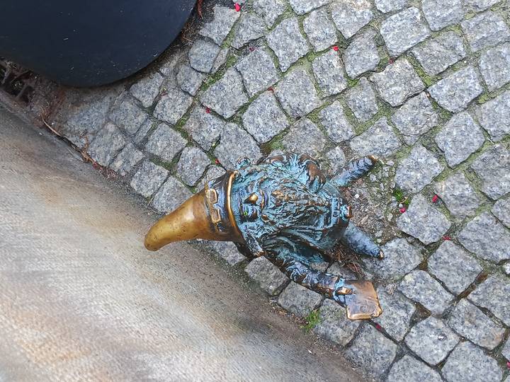 Close-up of a bronze dwarf statue with a golden hat standing on cobblestone pavement.