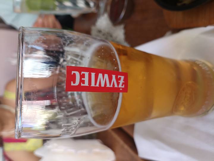 Close-up of a chilled glass of Żywiec beer on a table with a blurred diner in the background.