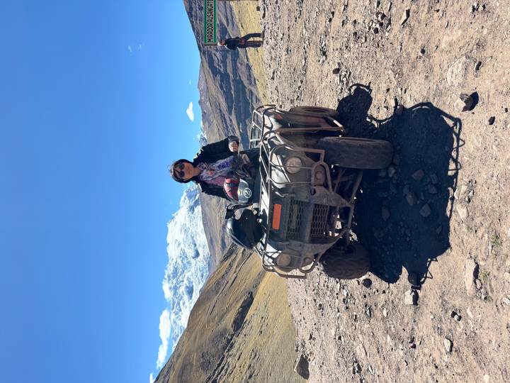 Person riding an ATV on a rugged mountain trail with snow-capped Andes peaks in the background.