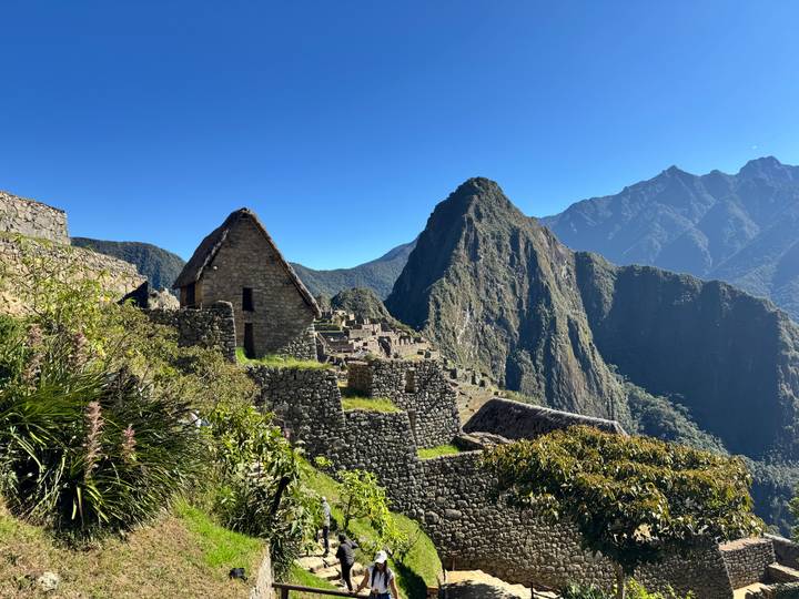 Classic stone structures and terraces of Machu Picchu set against steep green mountains under a vivid sky.