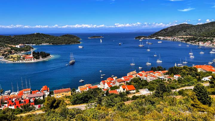 Panoramic bay dotted with sailboats and quaint coastal villages with red-tile roofs on a clear day