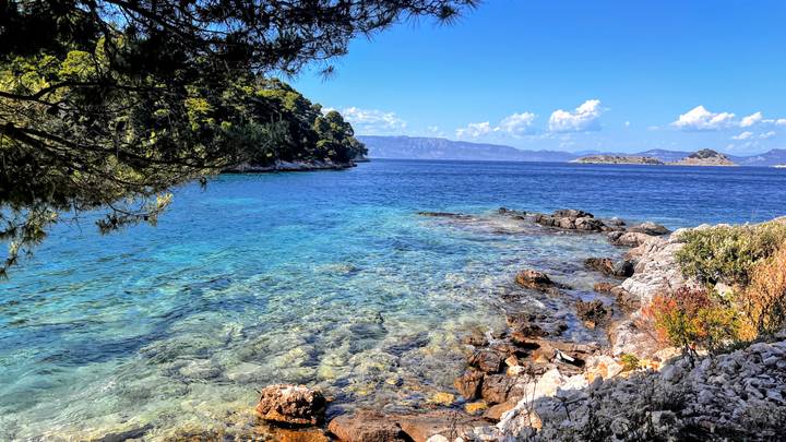 Crystal-clear turquoise cove with rocky shoreline and forested islands in the distance