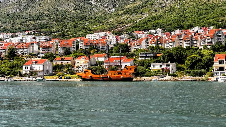 Traditional wooden galleon moored in front of a Croatian seaside town with terracotta rooftops