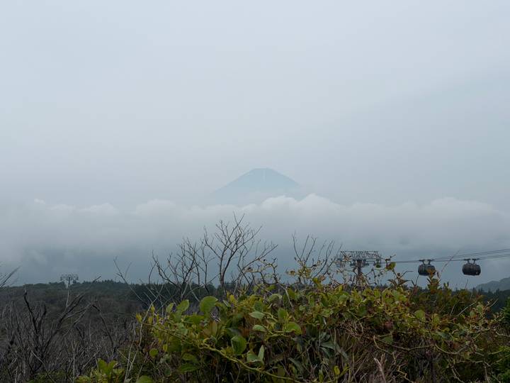Distant peak of Mount Fuji barely visible above heavy clouds with cable-car towers in foreground.