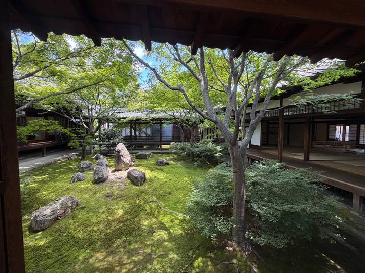 Tranquil moss-covered Zen garden with rocks, manicured trees and wooden corridors surrounding it.