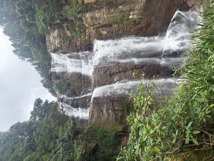 Tall multi-tiered waterfall cascades over rocky cliffs surrounded by lush jungle vegetation.