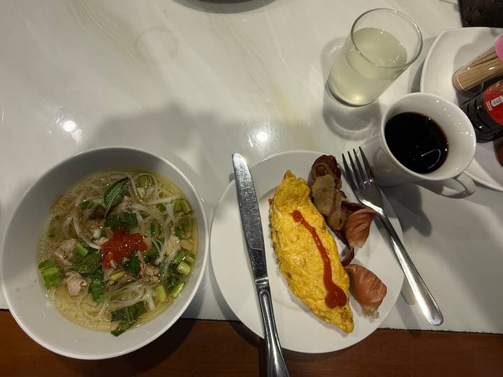 Overhead view of Vietnamese pho soup and omelette breakfast with coffee on a white table.