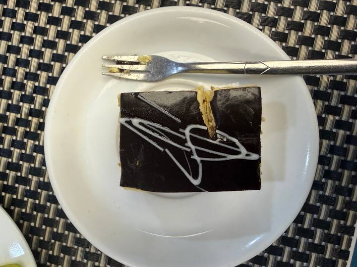 Close-up of a small chocolate pastry square with decorative white icing next to a fork.