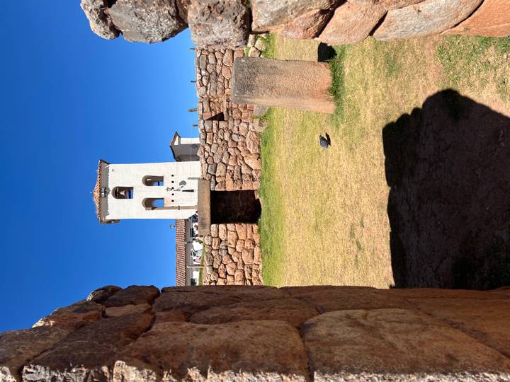 White colonial church tower rises above Inca stone walls under deep blue Andean sky