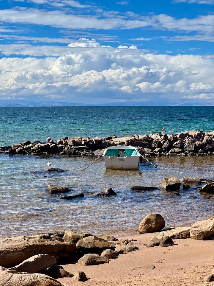 Small white boat moored to rocks on the clear blue waters of Lake Titicaca