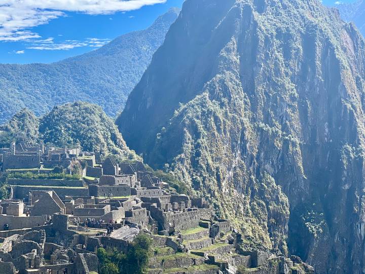 Steep green cliff of Huayna Picchu towers above the stone structures of Machu Picchu