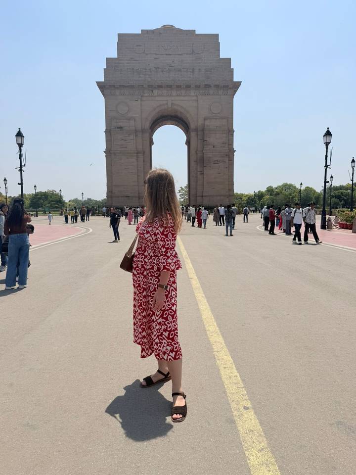 A visitor poses near India Gate’s central boulevard amid crowds on a bright day in New Delhi.
