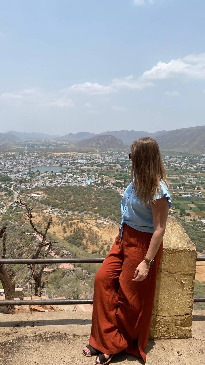 A woman looks out over a sprawling valley town, lake and surrounding arid hills from a high rocky vantage point.