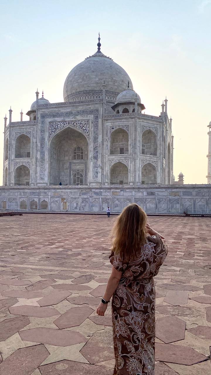 A visitor admires the marble façade of the Taj Mahal from its vast sandstone courtyard in soft early light.