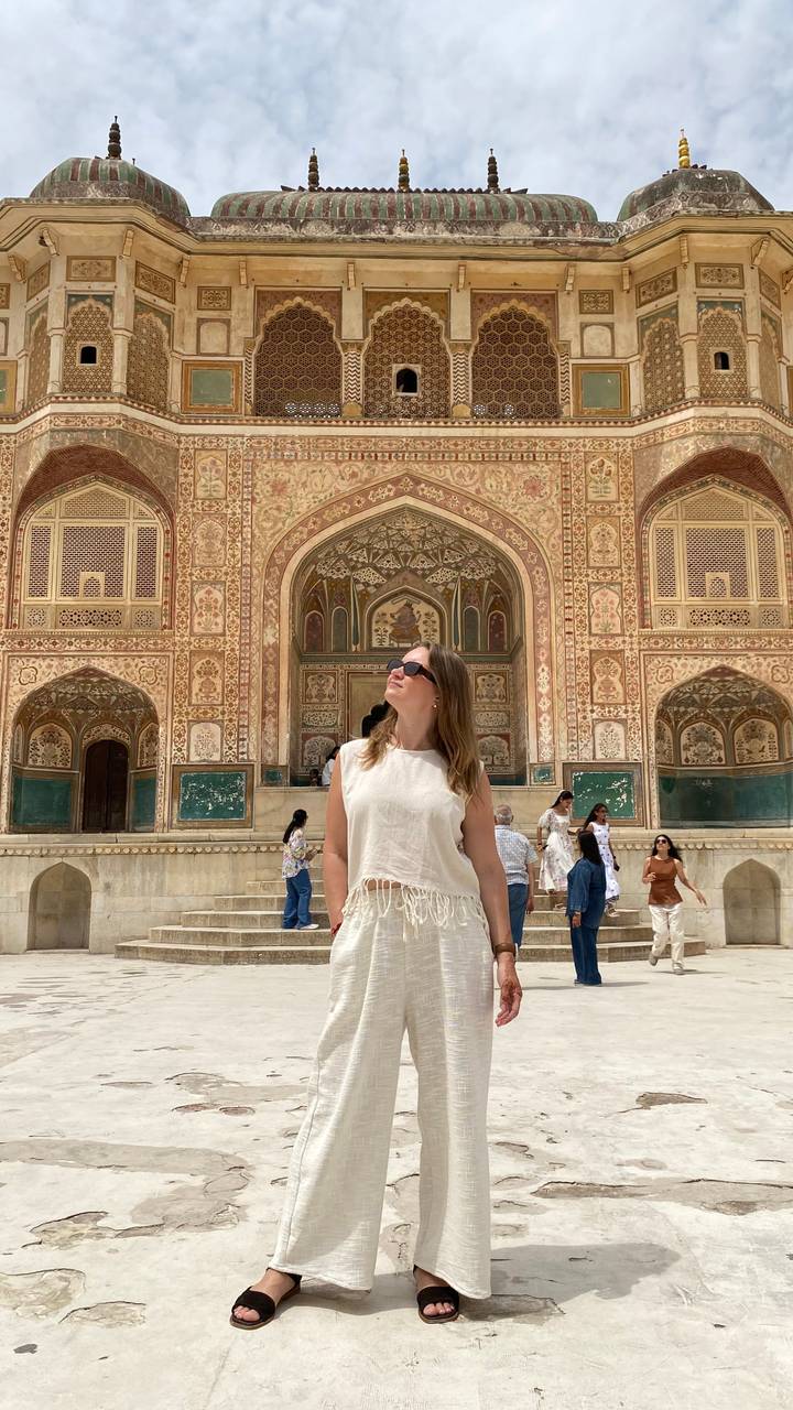 A traveler wearing sunglasses stands before the intricately painted Ganesh Pol gateway at Amber Fort in Jaipur.