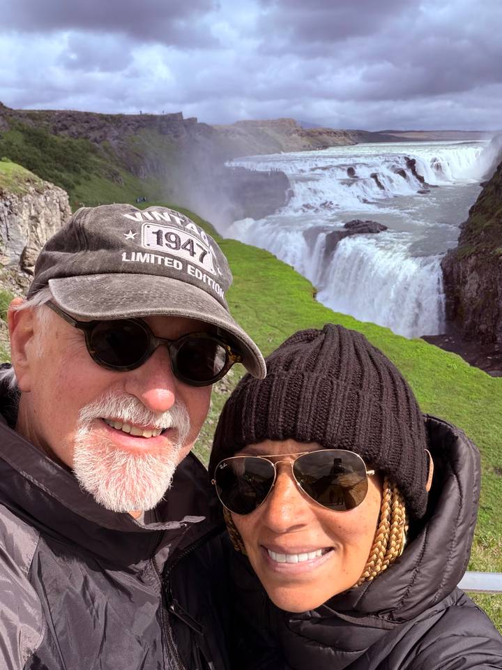 Couple taking a selfie with a wide powerful waterfall plunging into a green gorge
