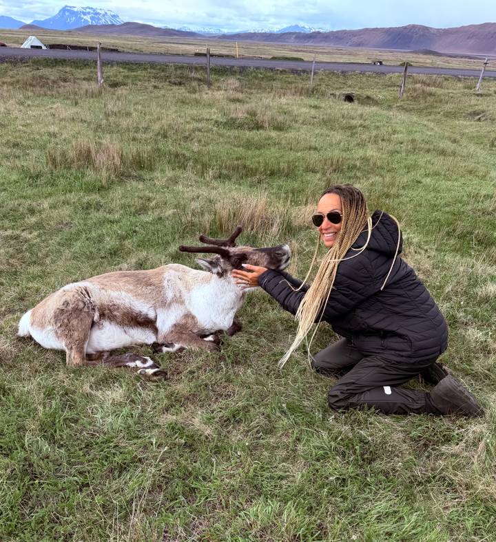 Traveler kneeling on grass while stroking a relaxed reindeer