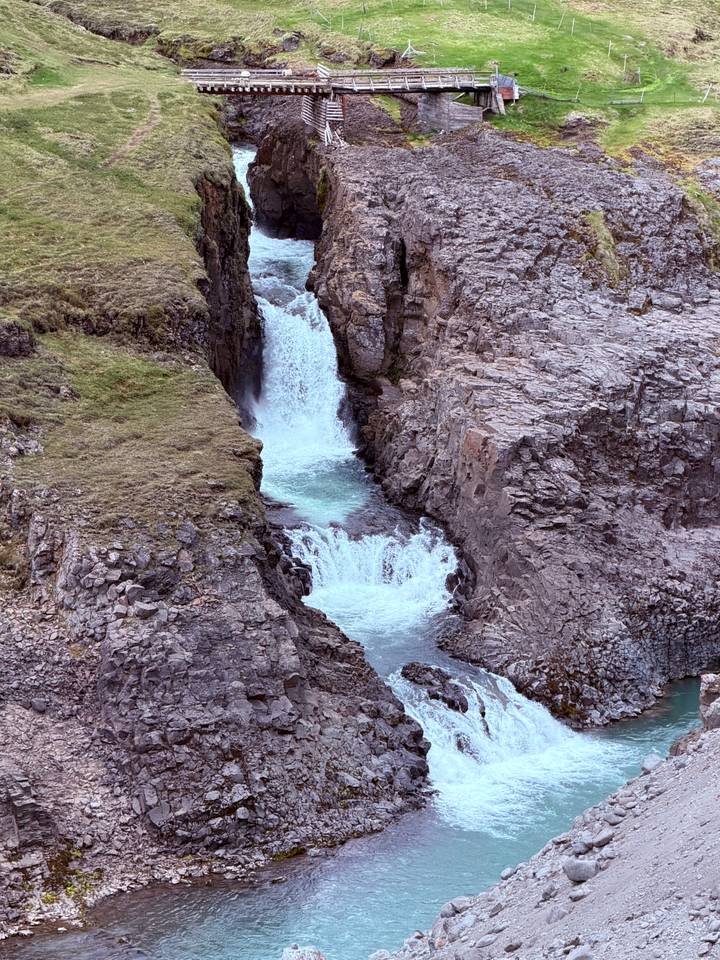 Narrow twin waterfalls dropping into a rocky gorge surrounded by tundra vegetation