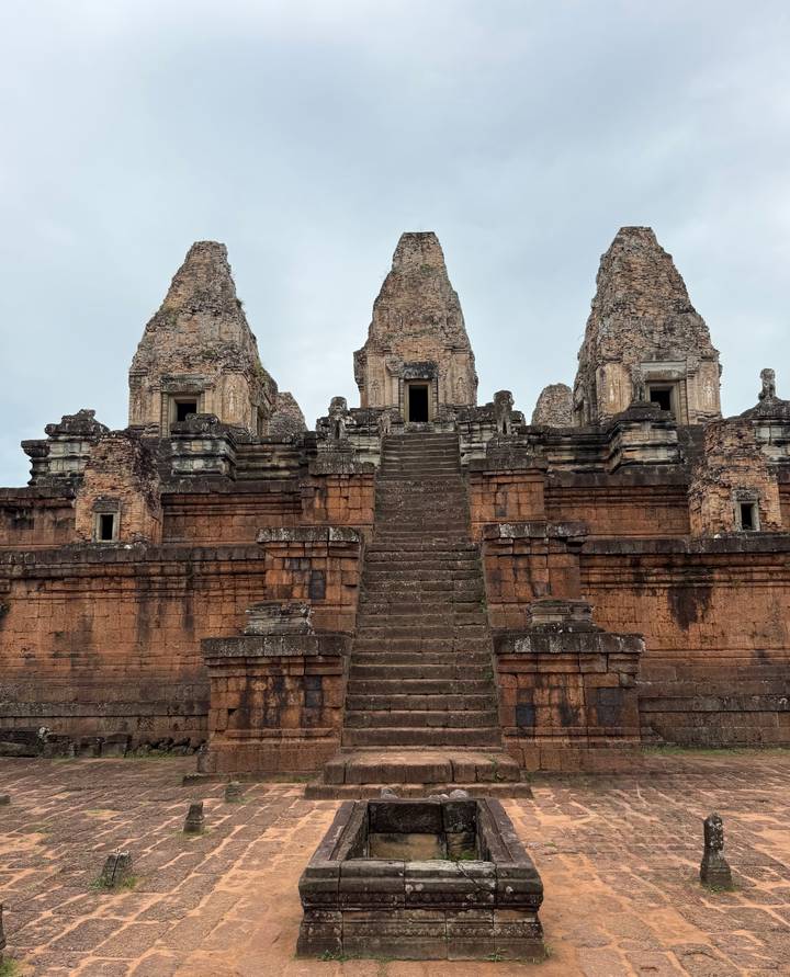 Ancient brick temple with three towers and steep central staircase under grey sky