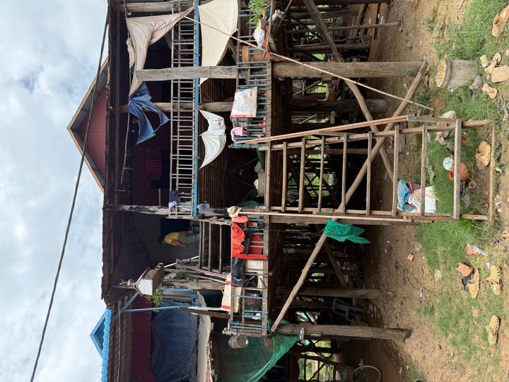 Weathered stilt house with clothes and tarps hanging, accessed by wooden ladder