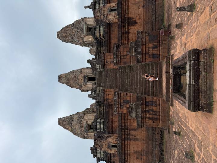 Wide view of temple staircase with two visitors seated halfway up under cloudy skies