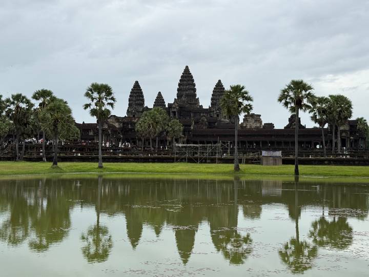 Iconic silhouette of Angkor Wat reflected in a still pond with palm trees in foreground