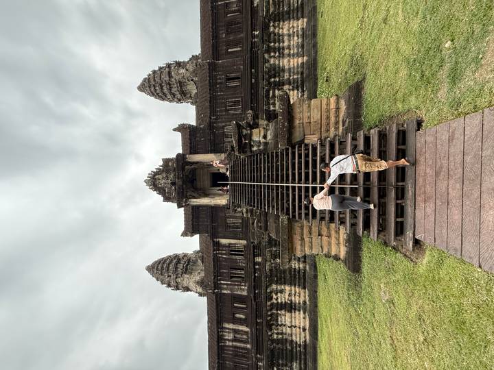 Elderly visitors climbing steep wooden steps with handrail toward an Angkor Wat doorway