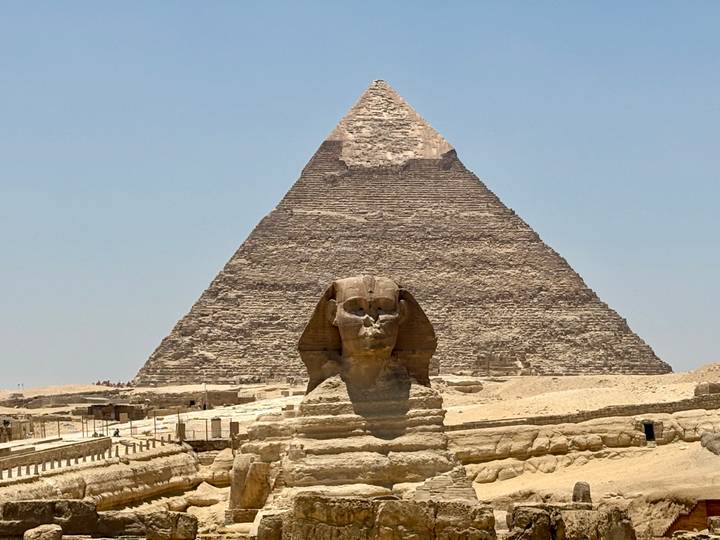 The Great Sphinx sits before the towering Great Pyramid on a bright desert day.