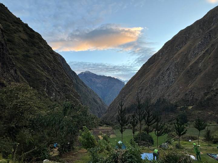 V-shaped green valley at dawn with snow-capped Andean peaks under colorful clouds.