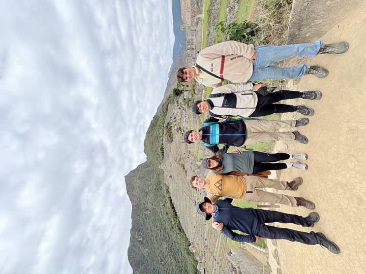 Six hikers posing together in front of stone terraces of Machu Picchu.