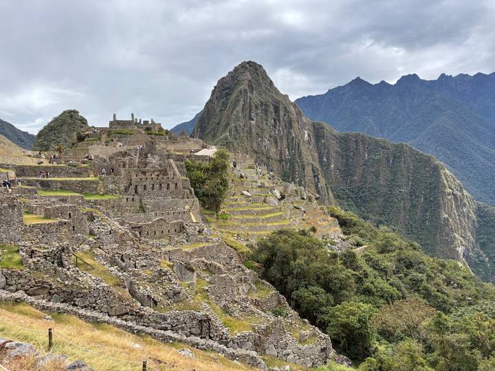 Panoramic view of Machu Picchu citadel perched on green mountains against misty peaks.