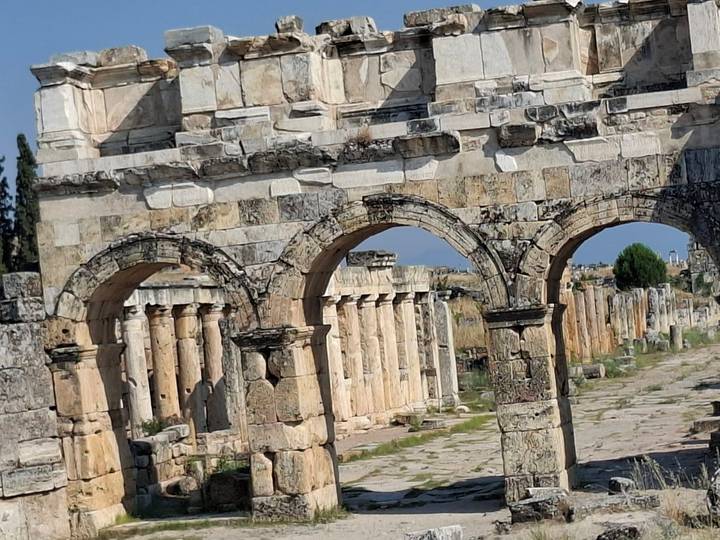 Angled view of arched Roman ruins and colonnaded street under clear blue sky.