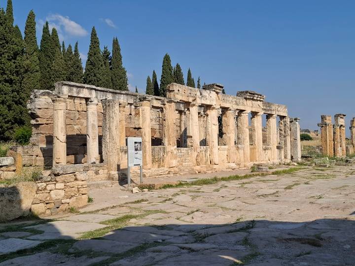 Stone columns of an ancient Roman bath complex framed by tall cypress trees.
