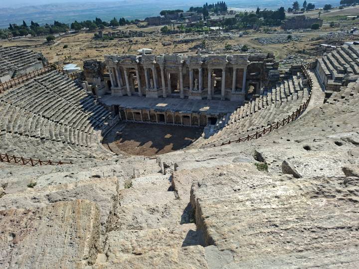 Panoramic view down into a well-preserved Roman amphitheater with tiered stone seating.
