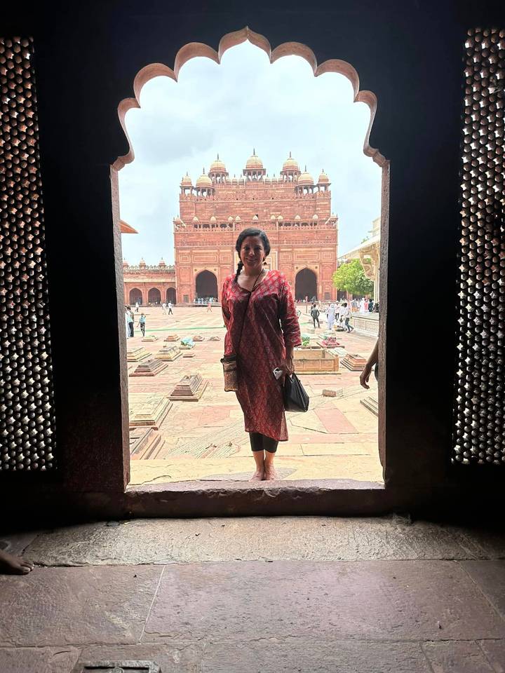 Traveller framed in a stone doorway looking onto the vast red sandstone courtyard of a Mughal monument.