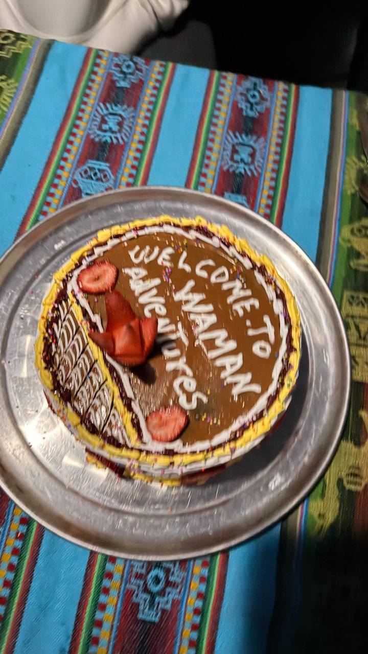 Chocolate frosted celebration cake with the words 'Welcome to Waman Adventures' and strawberries on a tray.