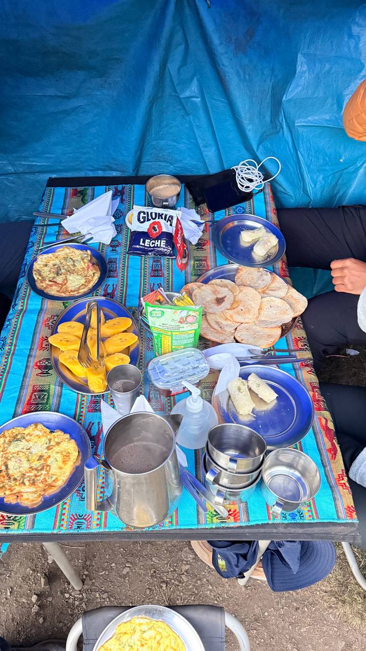 Breakfast spread on colourful Andean tablecloth with omelette, fruit and bread beside camper.