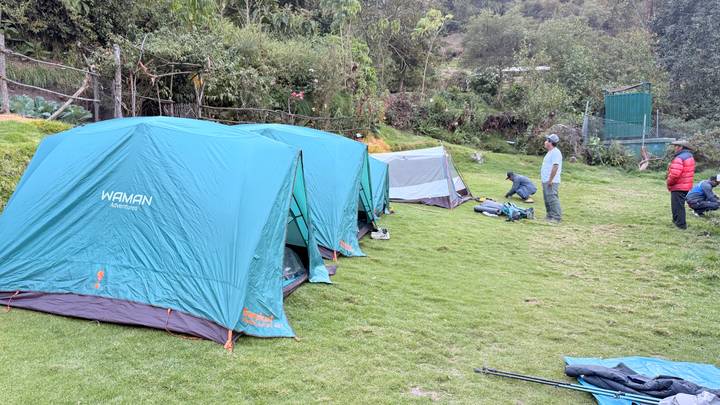 Turquoise Waman expedition tents pitched on grassy campsite with porters arranging gear.