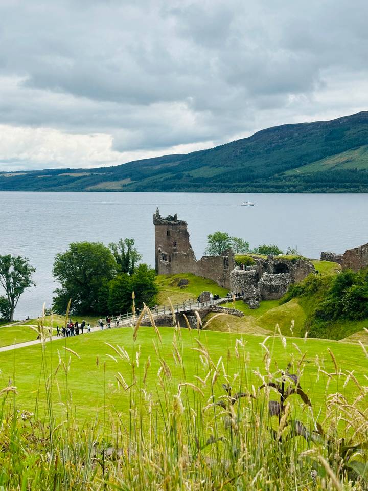 Historic Urquhart Castle ruins overlook the calm waters of Loch Ness with a tour boat passing by.