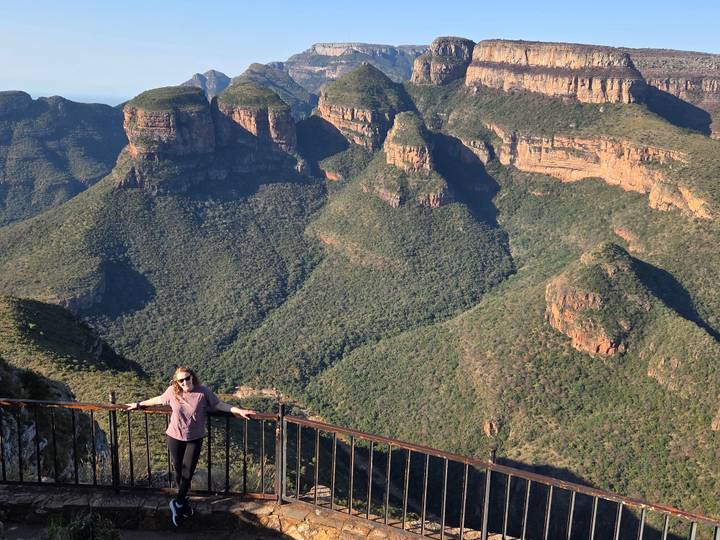 Woman leaning on a viewing railing high above the dramatic green peaks of Blyde River Canyon.