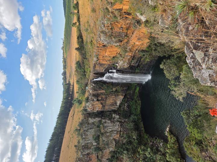 Tall waterfall plunging into a circular pool surrounded by orange cliffs and green countryside.