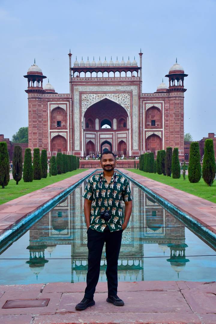 Traveller stands by the long reflecting pool facing the ornate main gate of the Taj Mahal complex.