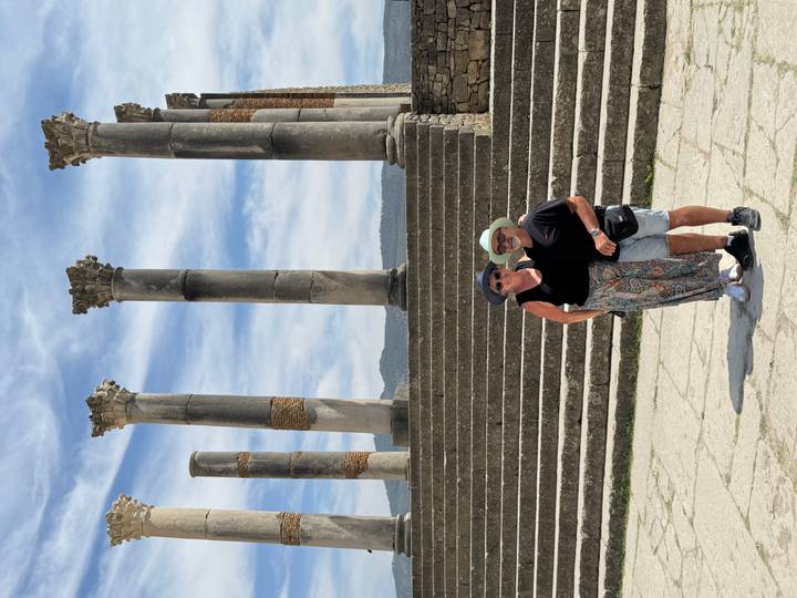 Smiling couple standing before ancient stone columns and steps at the Roman ruins of Volubilis.
