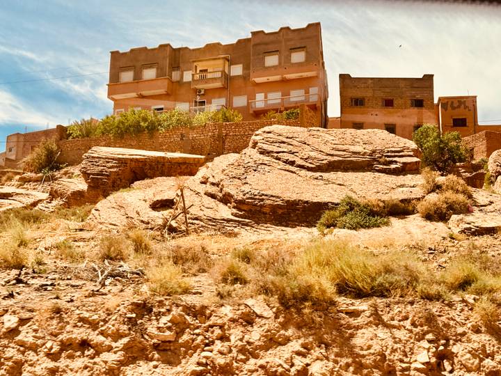 Arid rocky hillside with layered stone outcrops and small desert town buildings above.