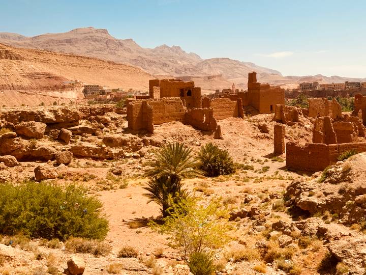 Ruined adobe fortress structures scattered across a rocky desert valley with mountains behind.