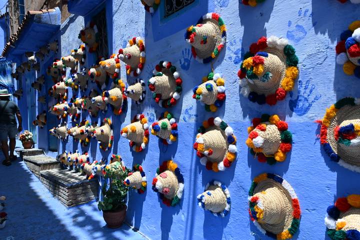 Wall lined with colorful pom-pom straw hats in the blue streets of Chefchaouen.