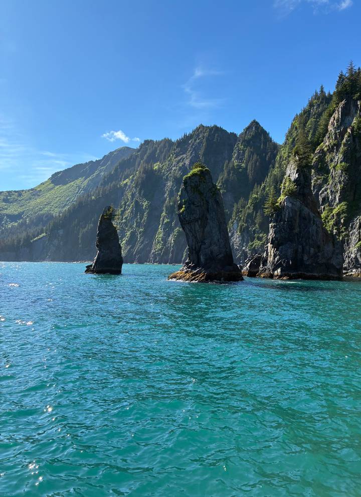 Turquoise ocean waters with tall rocky sea stacks and lush cliffs near Seward, Alaska.