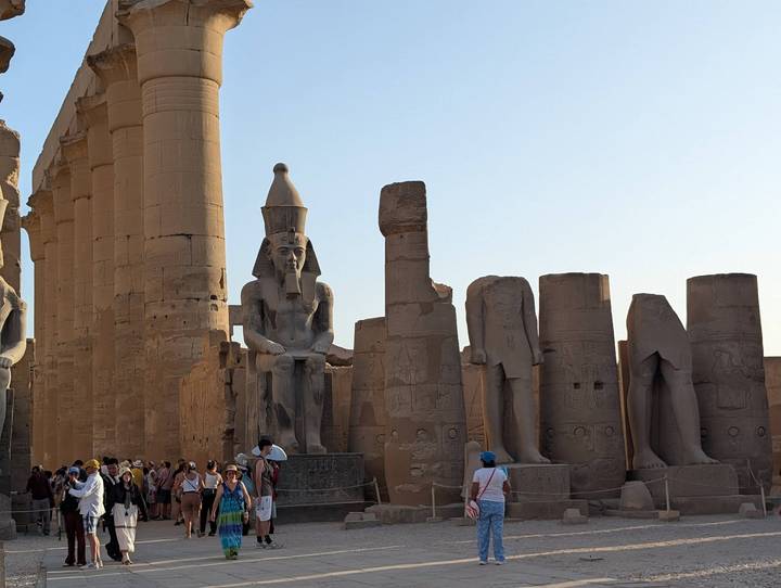 Visitors explore the grand columns and seated pharaoh statues of Luxor Temple under soft evening light.